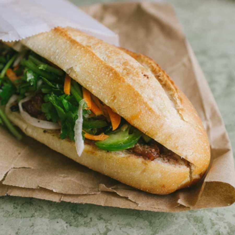 A vendor preparing fresh banh mi sandwiches with various ingredients in Hanoi