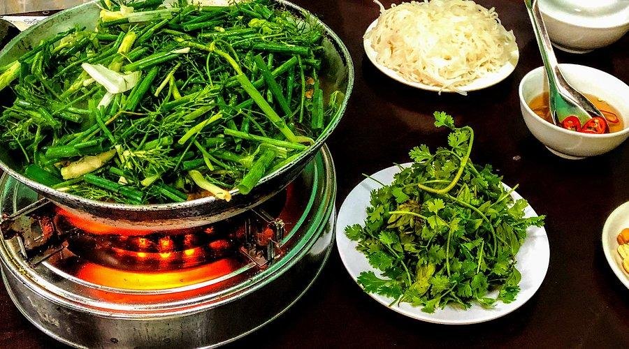 Traditional Cha Ca fish dish being prepared at a table in Hanoi with fresh herbs and dipping sauces