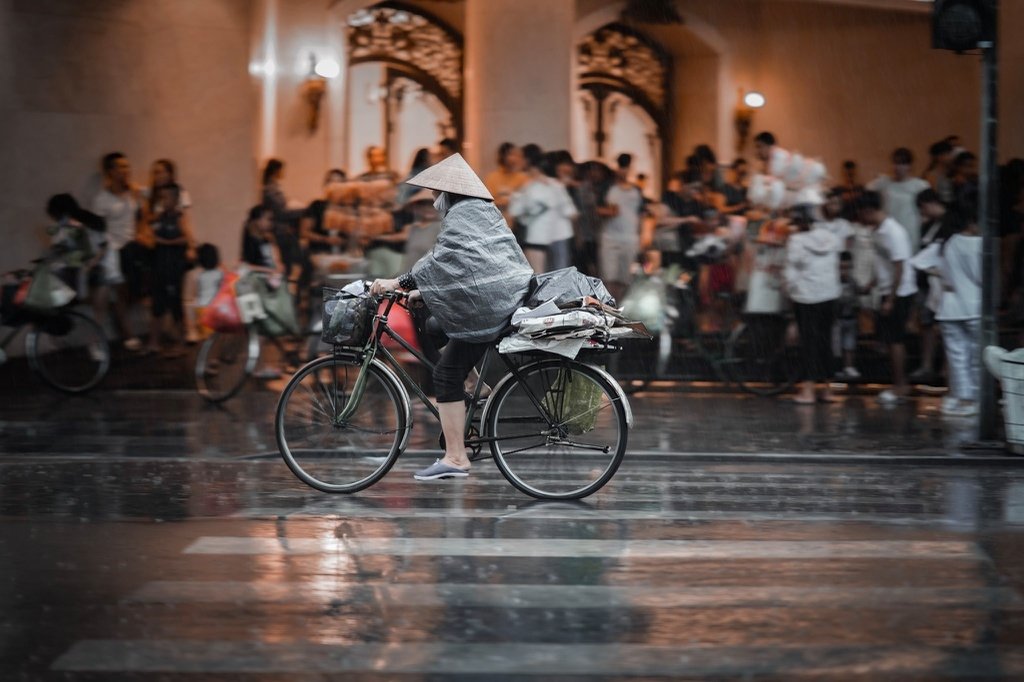 Cyclists riding through Hanoi streets after summer rain with wet reflective surfaces