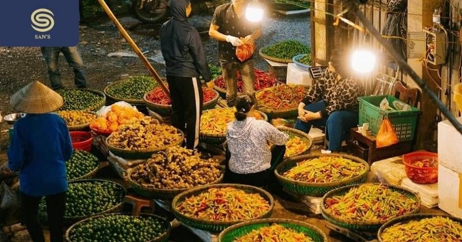Tourists exploring fresh vegetables and herbs at a traditional Hanoi market