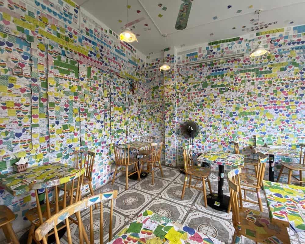 Interior of The Note Coffee shop with walls covered in colorful sticky notes from visitors around the world