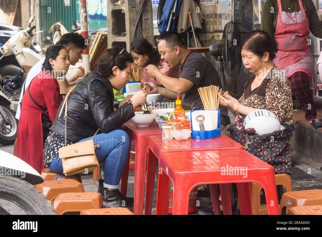 Busy food street in Hanoi Old Quarter with various food stalls and diners on small plastic stools