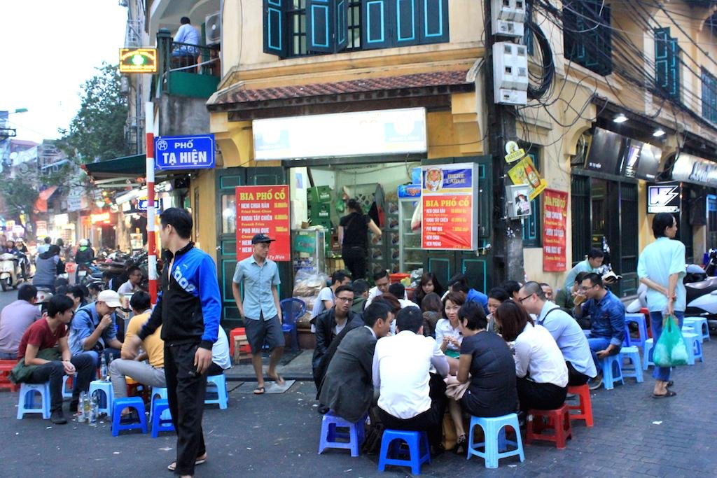Crowded beer corner with people sitting on plastic stools enjoying drinks